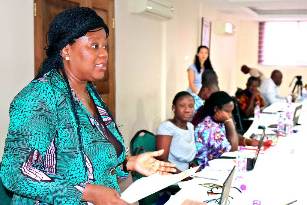 female presenter standing up at table of participants and talking